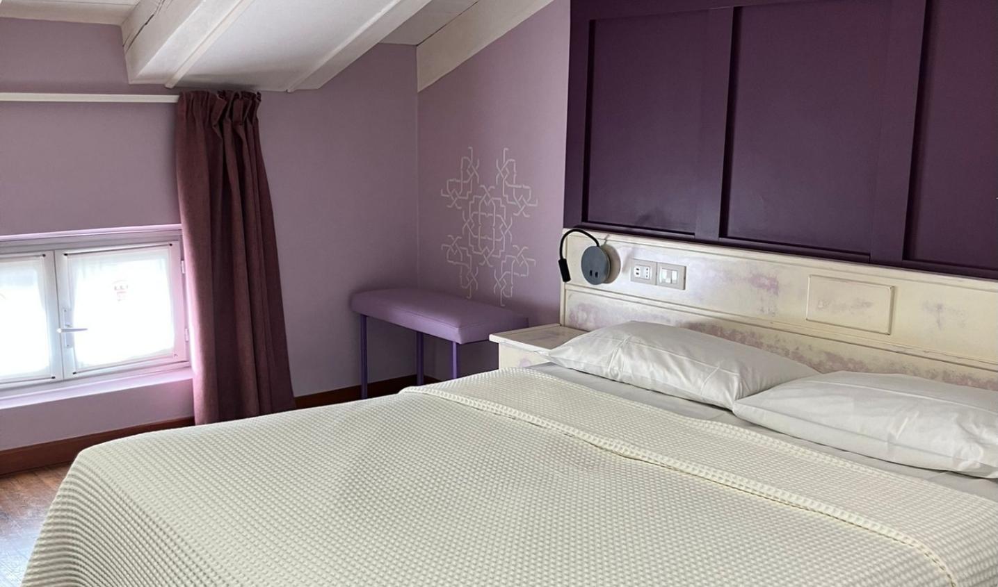 Camera da letto con pareti viola, letto matrimoniale e finestra bassa.