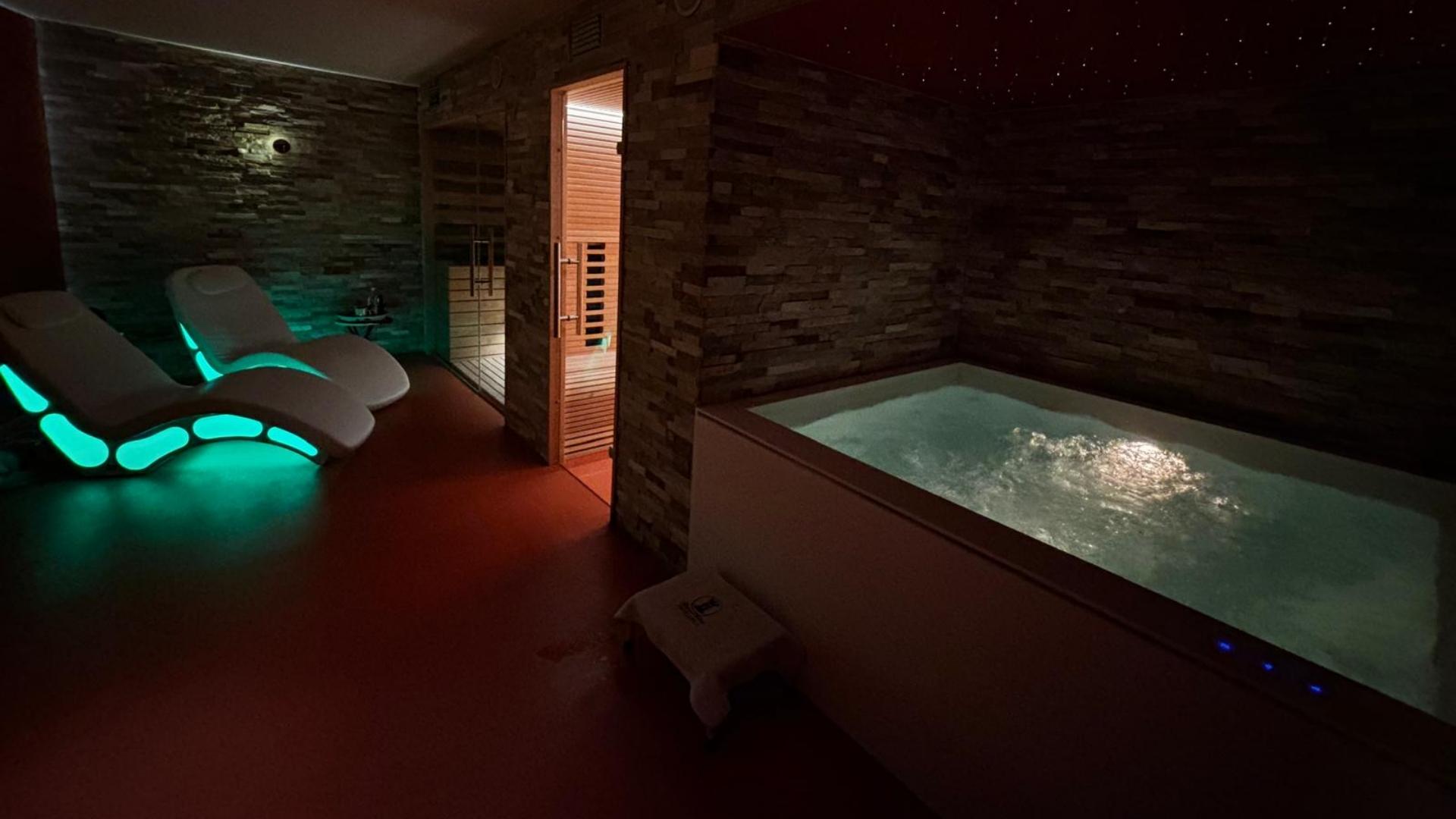 Spa con lettini luminosi, sauna e vasca idromassaggio in un ambiente rilassante.