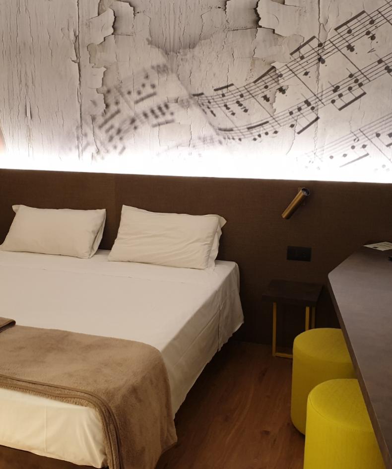Camera moderna con decorazione musicale, letto matrimoniale e sgabelli gialli.