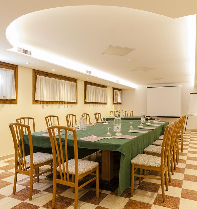 Sala riunioni elegante con tavolo verde, sedie in legno e proiettore.
