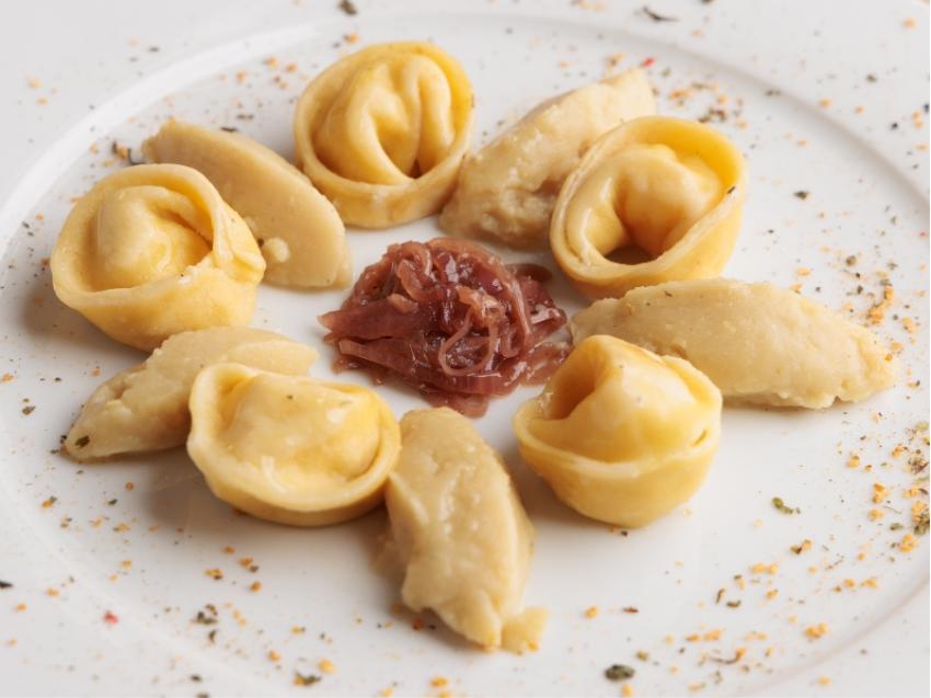 Tortellini con cipolla caramellata al centro, serviti su un piatto con spezie.