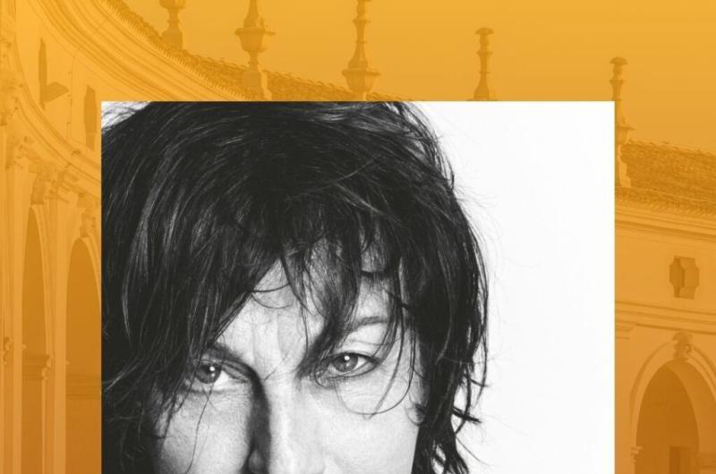 Ritratto intenso di Gianna Nannini su sfondo architettonico caldo.