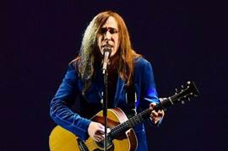 Cantante appassionato suona la chitarra con intensità, indossando un abito blu.