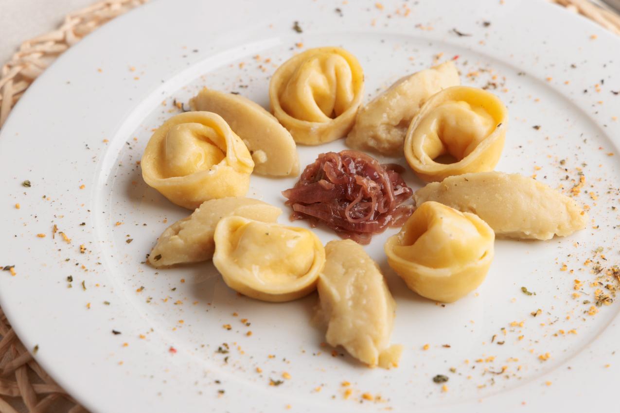 Tortellini con cipolle caramellate al centro, su piatto bianco con spezie.