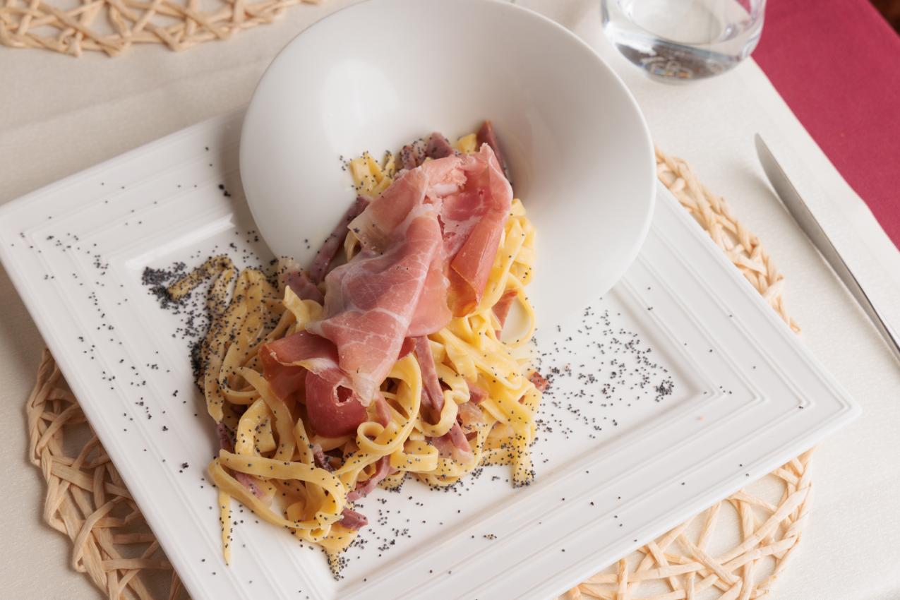 Tagliatelle con prosciutto crudo e semi di papavero su piatto elegante.