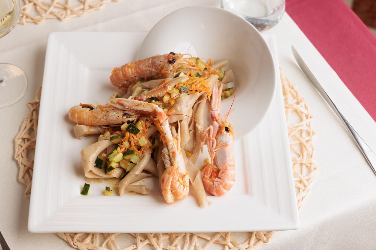 Tagliatelle con scampi e zucchine su piatto bianco, servite elegantemente.