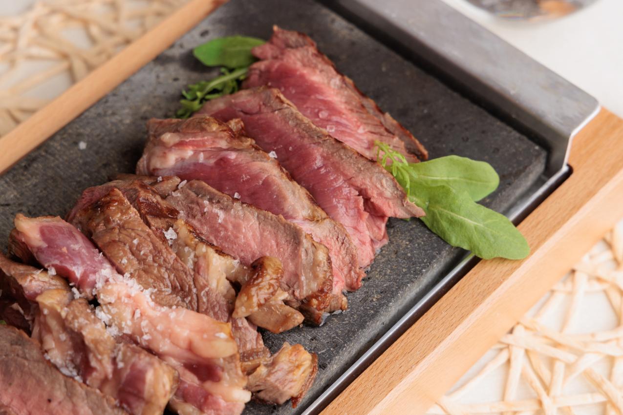 Tagliata di carne su pietra calda, guarnita con erbe fresche e sale grosso.