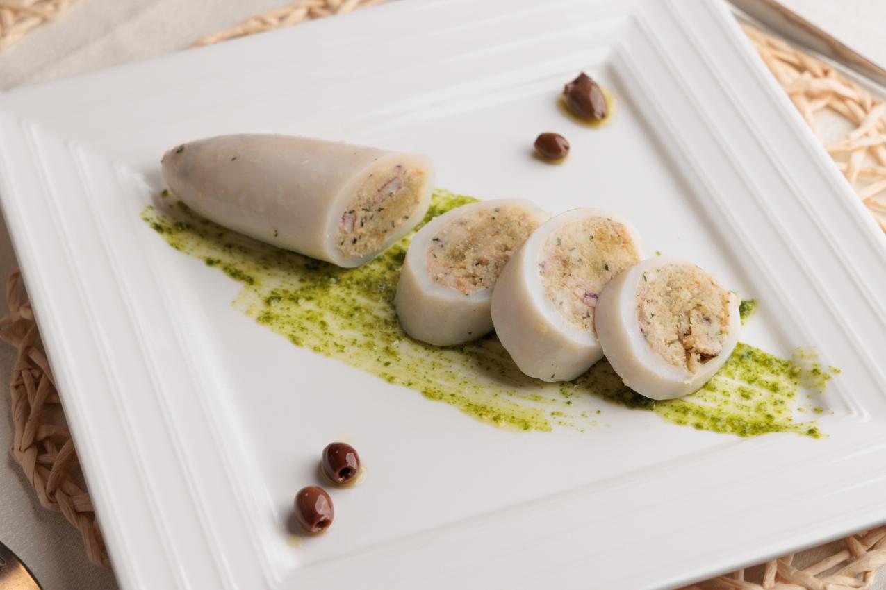 Calamari ripieni su salsa verde con olive su piatto bianco elegante.