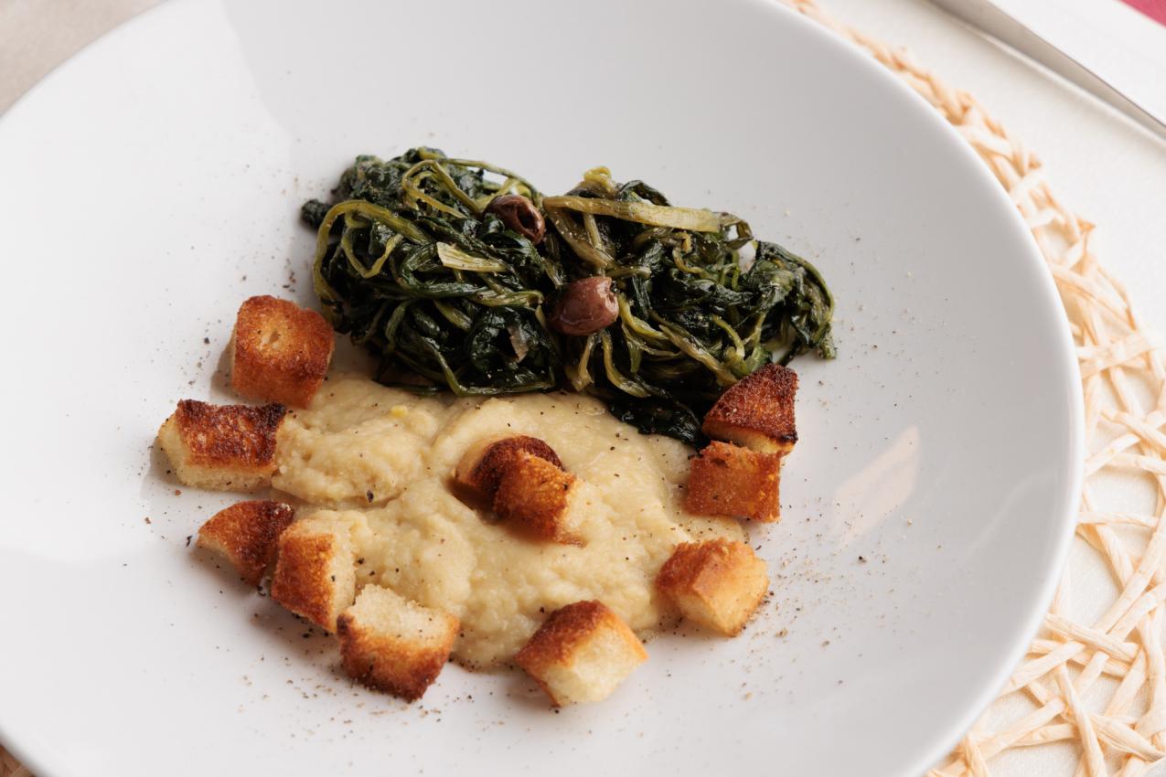 Purea di fave con cicoria e crostini su piatto bianco.