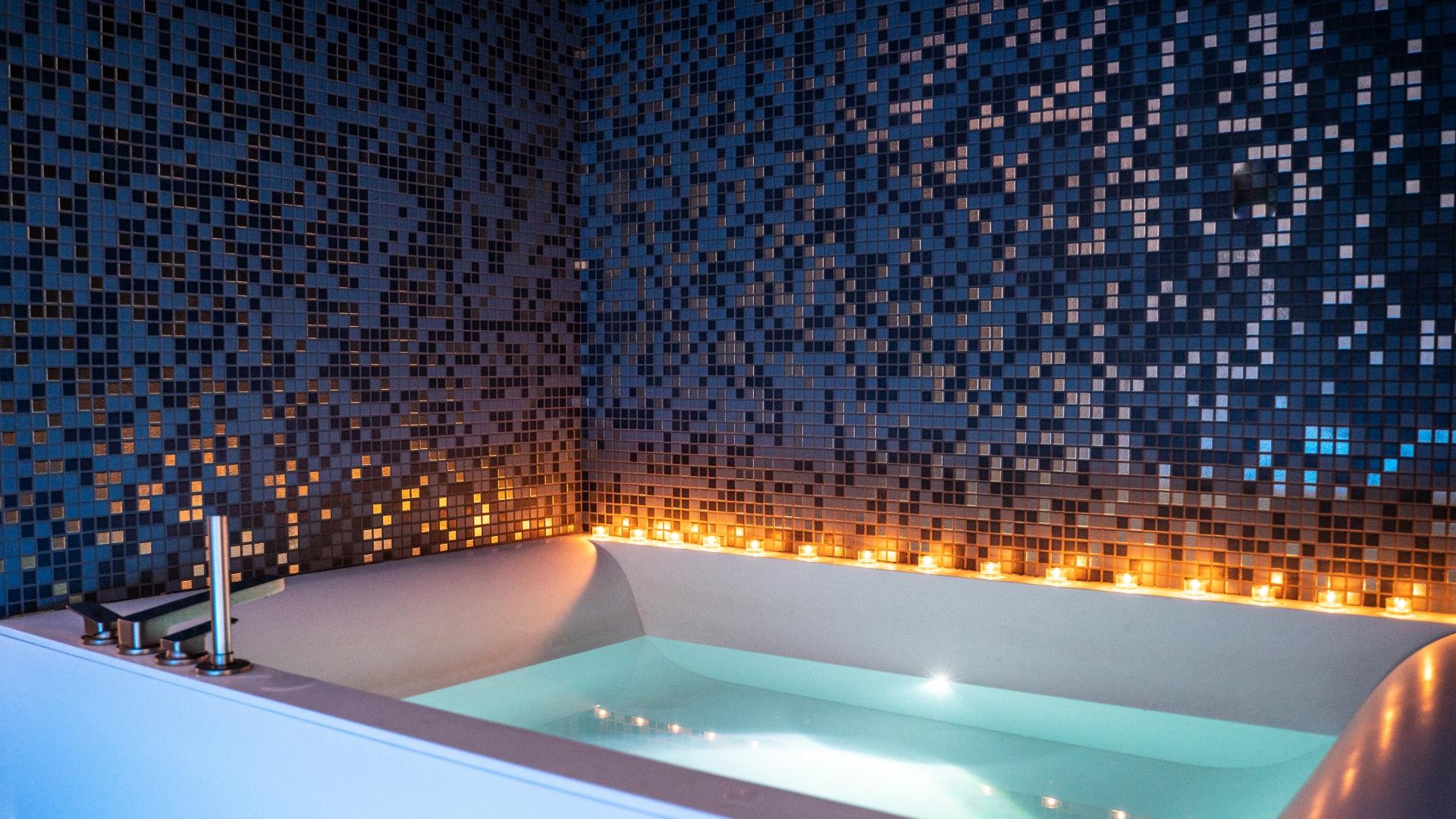 Vasca da bagno con mosaico blu e candele per un'atmosfera rilassante.