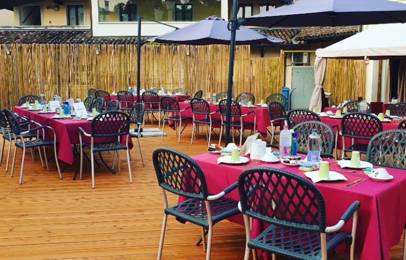 Ristorante all'aperto con tavoli apparecchiati e ombrelloni su pavimento in legno.