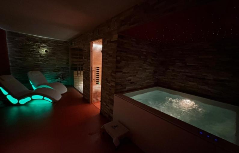 Spa con lettini illuminati, sauna e vasca idromassaggio in ambiente rilassante.