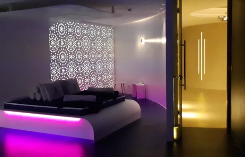 Stanza moderna con illuminazione soffusa, divano elegante e pannello decorativo luminoso.