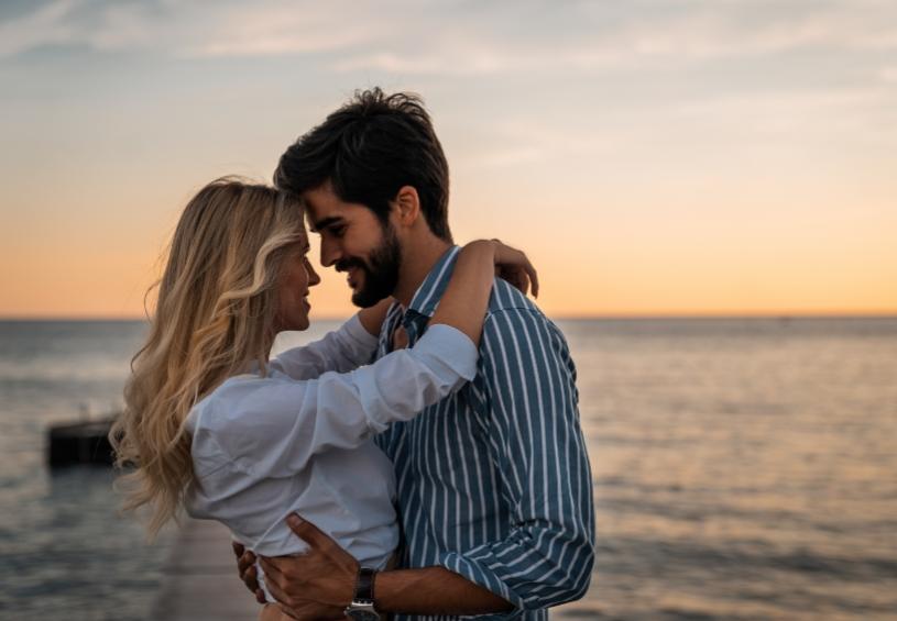 Coppia abbracciata al tramonto, con il mare sullo sfondo.