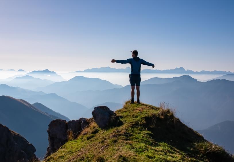 Persona in cima a una montagna, braccia aperte, panorama mozzafiato.