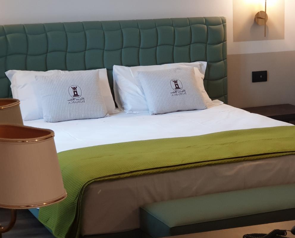 Camera moderna con letto matrimoniale, testiera verde e coperta verde chiaro.